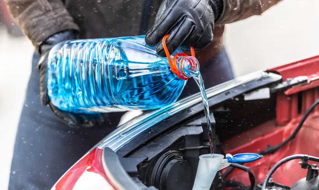 gettyimages-1441895768 A male driver wearing gloves pours antifreeze into the tank to spray the windshield during a snowstorm.